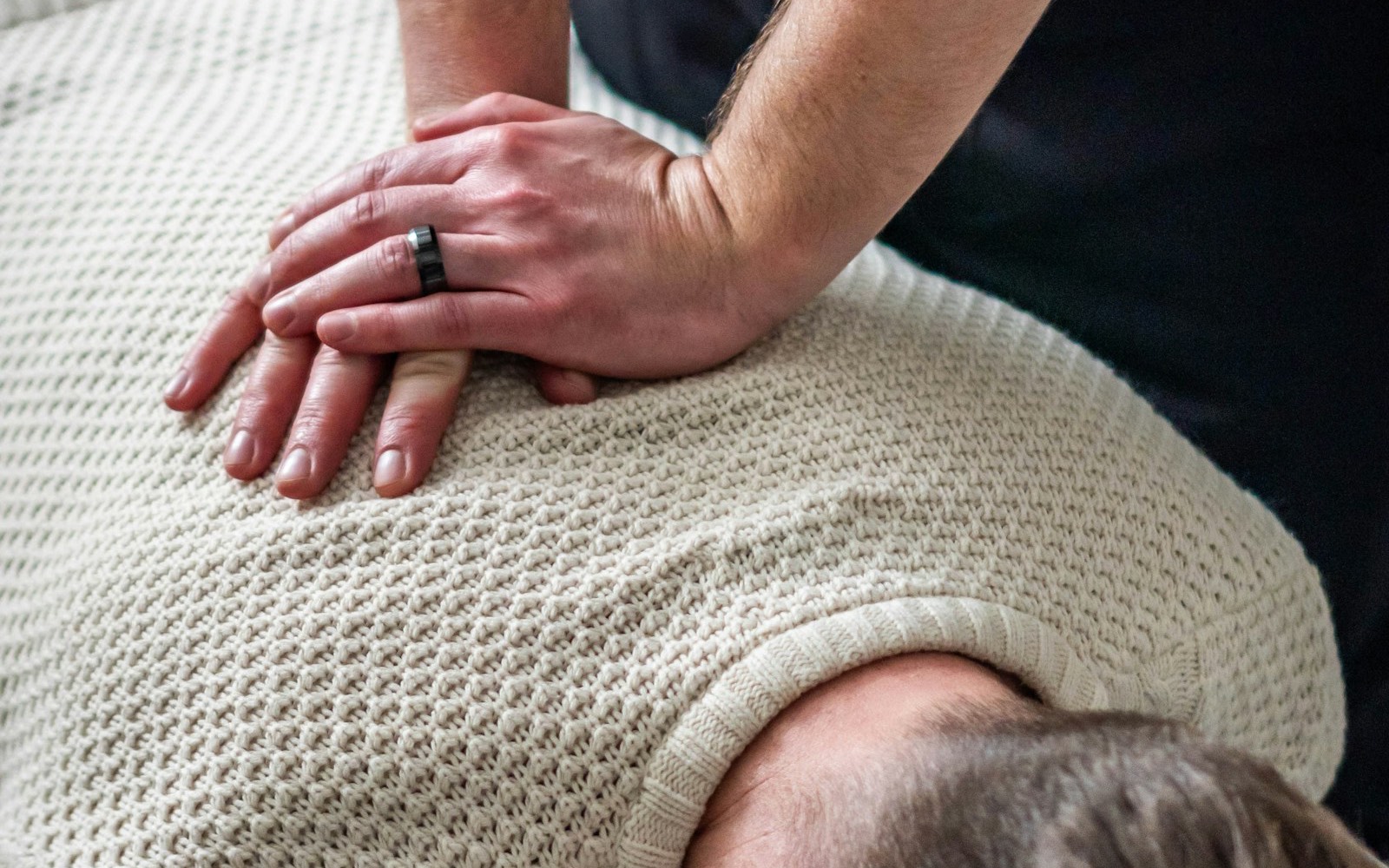 Ostéopathe appliquant un soin manuel sur le dos d'un patient allongé, mains superposées, ambiance chaleureuse.